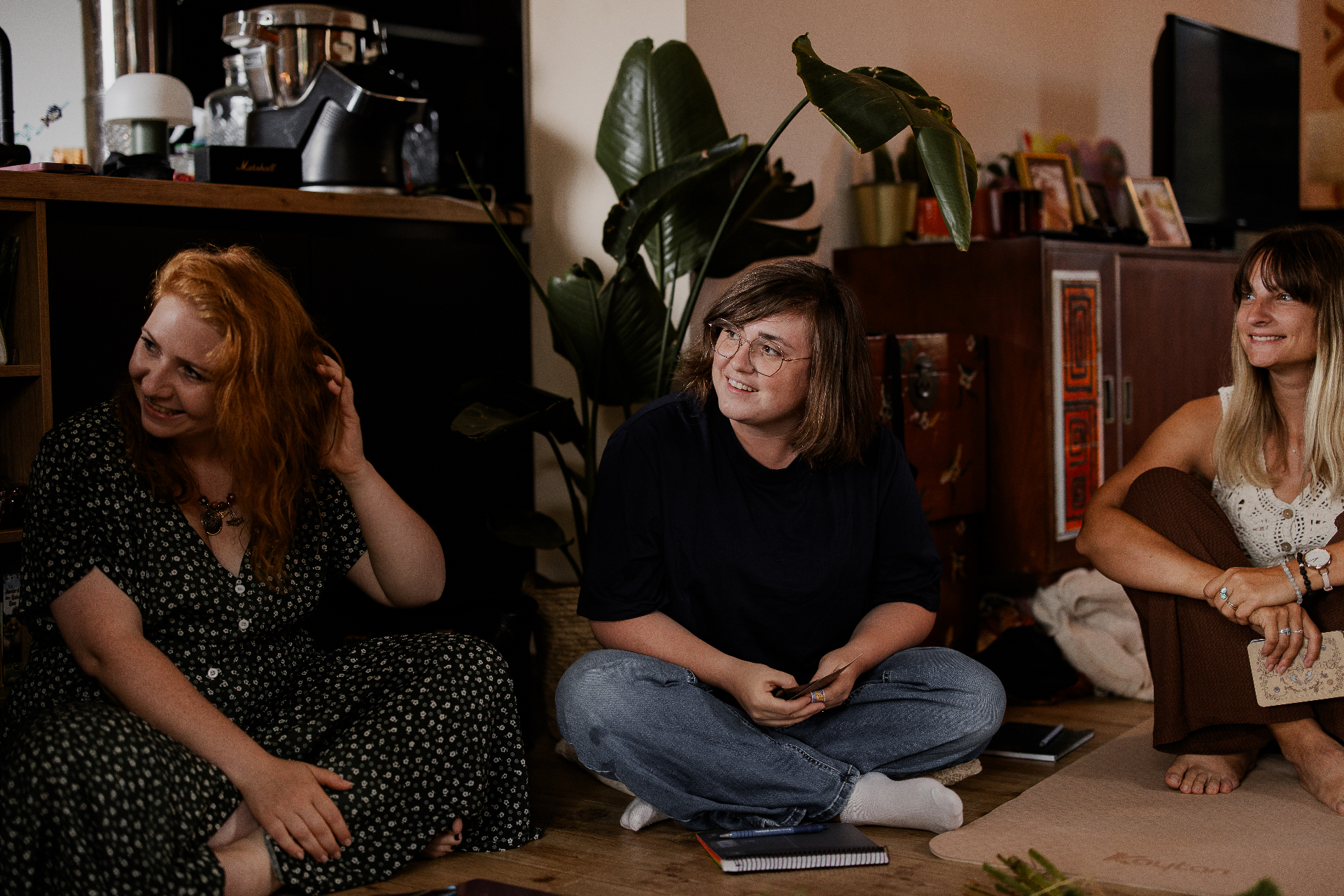 Trois participantes assises au sol, souriantes, lors d'un cercle en intérieur